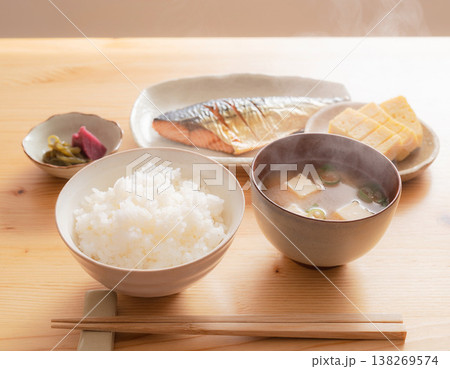 朝の光が差し込む木製テーブルの上の美味しそうなおかずと味噌汁とご飯 138269574