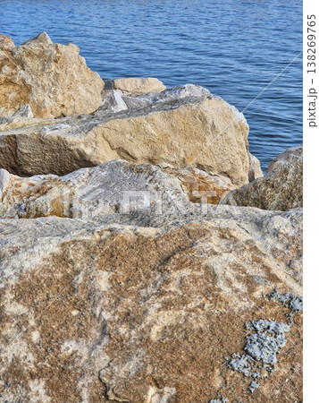 sea stones on the beach. Large limestone rocks on the shore with blue rippled water in the background. 138269765