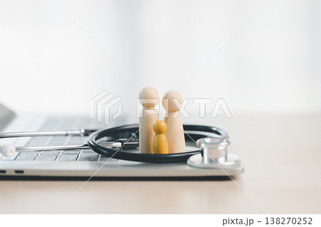 Wooden family figures on laptop with stethoscope and copy space, symbolizing telemedicine, family healthcare, online medical consultation and digital health insurance protection for telehealth. 138270252