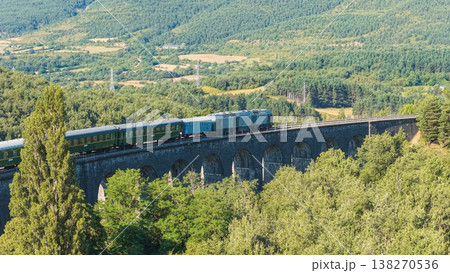 Vintage train crossing stone viaduct in mountain landscape 138270536