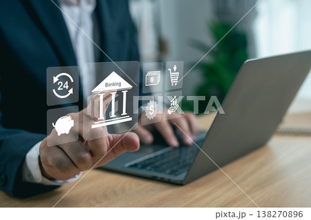 Business professional using digital bank app with various financial icons on virtual screen and laptop in modern workspace setting to manage accounts Business professional using digital bank app with various financial icons on virtual screen and laptop in modern workspace setting to manage accounts 138270896