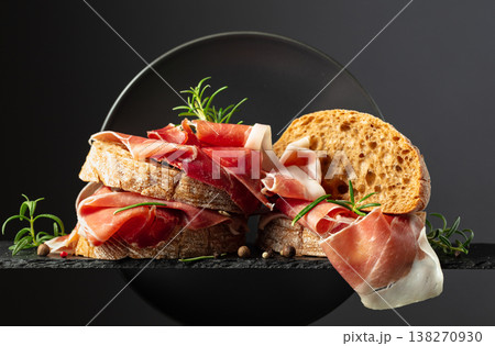 Ciabatta with prosciutto and rosemary on a black background. 138270930