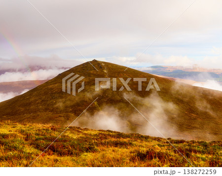 Highland mountain peak glows golden as mist covers its lower slopes beneath a partly cloudy sky. Highland mountain peak glows golden as mist covers its lower slopes beneath a partly cloudy sky. 138272259