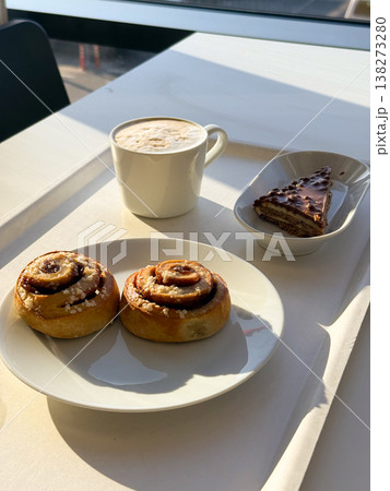 Coffee cup with foam and pastries with cake slice on tray in sunlight. Relaxation moment, cafe lifestyle, leisure break, enjoyment, calm atmosphere, everyday pleasure 138273280