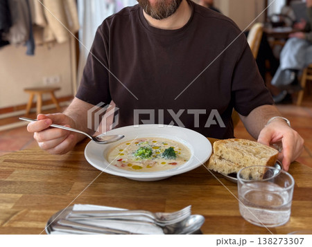 Close-up Man eating creamy broccoli soup served in white plate on wooden cafe table. Comfort food, healthy lunch concept and modern restaurant dining presentation. 138273307