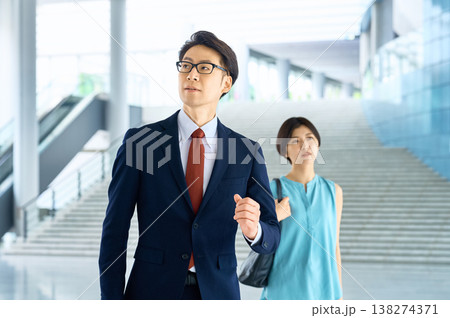 オフィスビルで前を見据えて歩く自信に満ちた日本人ビジネスマンと女性 オフィスビルで前を見据えて歩く自信に満ちた日本人ビジネスマンと女性 138274371