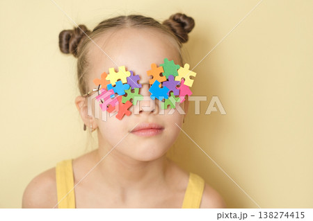 A child wearing glasses made from a variety of pieces of bright multicolored puzzles, demonstrating support and awareness of autism. A girl on a yellow studio background A child wearing glasses made from a variety of pieces of bright multicolored puzzles, demonstrating support and awareness of autism. A girl on a yellow studio background 138274415
