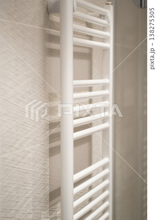 White modern heated towel rail hanging on a textured bathroom wall providing comfort and warmth in a contemporary and minimalist domestic interior 138275305