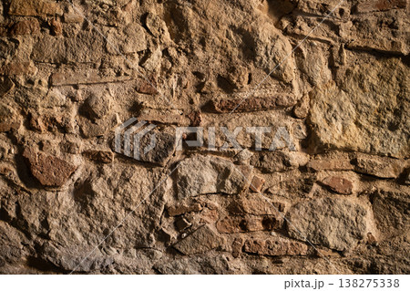 Rough ancient stone and rock wall showing weathered texture and uneven surface, forming a rugged historical background or natural pattern Rough ancient stone and rock wall showing weathered texture and uneven surface, forming a rugged historical background or natural pattern 138275338