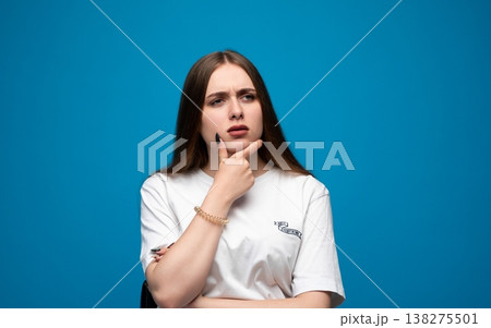 Young woman pondering a difficult decision, showing doubt and uncertainty while looking away on a blue background 138275501