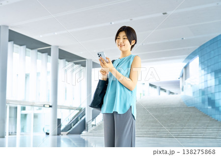 オフィスビルのエントランスでスマートフォンを操作しながら笑顔を見せる日本人女性 138275868