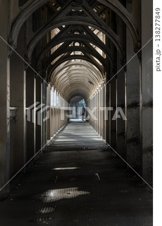 Within the shadowed belly of the bridge, a skeletal cathedral of iron stretches toward a distant, luminous exit. The atmosphere is one of quiet transition a moody, vaulted promenade where the grit of 138277849