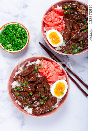 Gyudon Japanese beef with rice, pickled ginger, boiled egg slice, garnished with green onions, in a bowl with chopsticks, Gyudon Japanese beef with rice, pickled ginger, boiled egg slice, garnished with green onions, in a bowl with chopsticks, 138278910