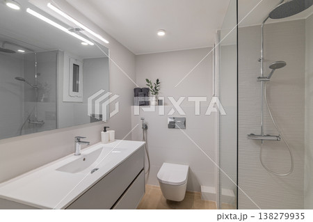 Modern bathroom with a sleek design. Features a white vanity, mirror, shower, and toilet. Bright lighting enhances the clean aesthetic. Modern bathroom with a sleek design. Features a white vanity, mirror, shower, and toilet. Bright lighting enhances the clean aesthetic. 138279935