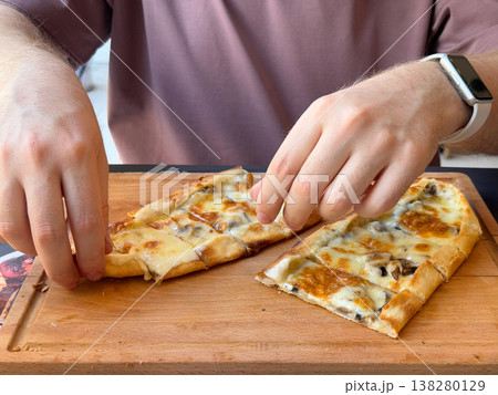 Hands reaching for cheese and mushroom pide slices on a wooden serving board. Casual meal interaction, shared lunch concept and appetizing restaurant food moment with human presence Hands reaching for cheese and mushroom pide slices on a wooden serving board. Casual meal interaction, shared lunch concept and appetizing restaurant food moment with human presence 138280129