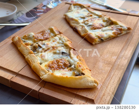 Cheese and mushroom pide slices photographed on a wooden board from a low angle. Menu presentation, baked comfort food appeal and cafe dining concept with artisanal flatbread texture Cheese and mushroom pide slices photographed on a wooden board from a low angle. Menu presentation, baked comfort food appeal and cafe dining concept with artisanal flatbread texture 138280130