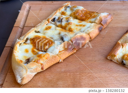 Closeup of a single cheese and mushroom pide slice with browned crust on a wooden board. Baked menu specialty, artisan flatbread detail and savory cafe food concept for restaurant promotion Closeup of a single cheese and mushroom pide slice with browned crust on a wooden board. Baked menu specialty, artisan flatbread detail and savory cafe food concept for restaurant promotion 138280132