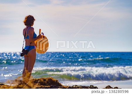 Woman in bikini with camera walk on beach Woman in bikini with camera walk on beach 138280596