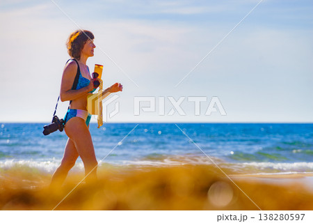 Woman in bikini with camera walk on beach 138280597