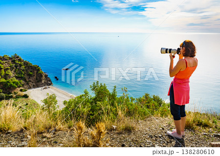 Woman with camera take travel photo on sea shore 138280610