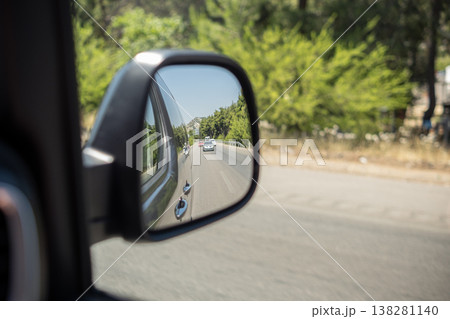Reflective View of a Road and Surrounding Greenery From a Car Side Mirror on a Sunny Day 138281140