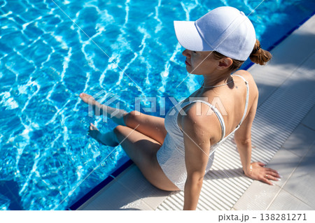 Woman Relaxing by the Poolside in a White Swimsuit, Enjoying the Sun and Cool Water During a Summer Day Woman Relaxing by the Poolside in a White Swimsuit, Enjoying the Sun and Cool Water During a Summer Day 138281271