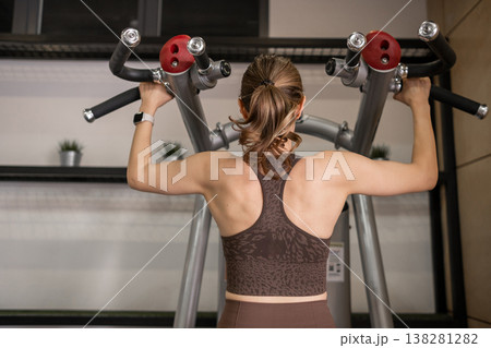 Strong Woman Performing Pull-Ups in Modern Gym During Afternoon Workout Session Strong Woman Performing Pull-Ups in Modern Gym During Afternoon Workout Session 138281282