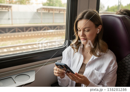 Young Woman Using Smartphone While Traveling on Train Near a Railway Station on a Sunny Day Young Woman Using Smartphone While Traveling on Train Near a Railway Station on a Sunny Day 138281286