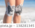Woman Applying Clay Mask on Knees at the Beach During Sunny Day for Skin Care and Relaxation 138281345