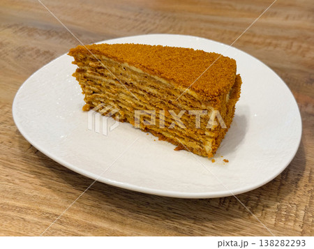 Honey cake slice on white plate with layered cream filling and crumb coating. traditional dessert, bakery product, pastry presentation, sweet indulgence, cafe serving, homemade recipe, comfort food Honey cake slice on white plate with layered cream filling and crumb coating. traditional dessert, bakery product, pastry presentation, sweet indulgence, cafe serving, homemade recipe, comfort food 138282293