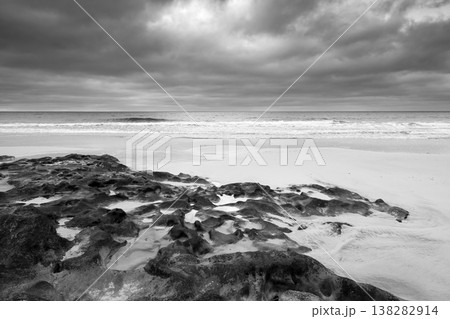 Black and white beach photography with rough black rocks, waves meeting the shore 138282914