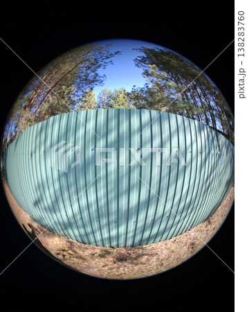 A green corrugated metal fence stands tall in front of a background of pine trees under a clear blue sky. This scene highlights themes of security and property protection. 138283760