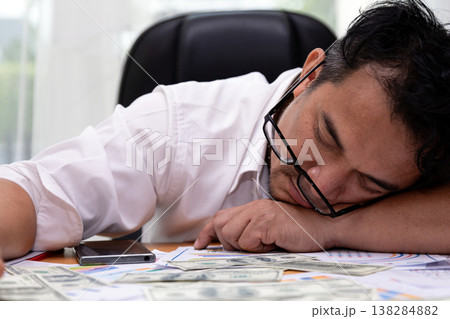 Exhausted businessman sleeping at desk with cash, financial reports and smartphone. Close-up shot burnout, money stress and business pressure in modern office Exhausted businessman sleeping at desk with cash, financial reports and smartphone. Close-up shot burnout, money stress and business pressure in modern office 138284882