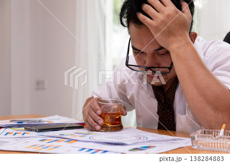 Stressed businessman holding whiskey glass while reviewing financial reports at desk. Close-up to money problems, burnout, debt pressure and emotional struggle in modern office Stressed businessman holding whiskey glass while reviewing financial reports at desk. Close-up to money problems, burnout, debt pressure and emotional struggle in modern office 138284883