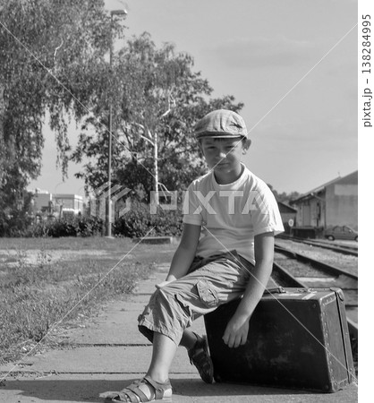 Young boy in cap sitting on vintage suitcase at train station, black and white 138284995