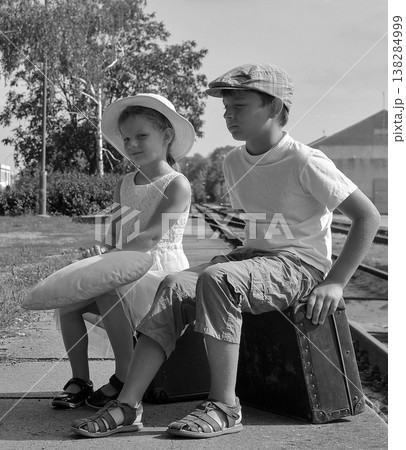 Two children in vintage clothing waiting on a train platform with luggage 138284999