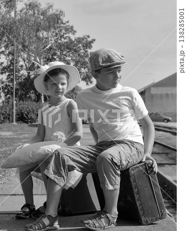 Children in vintage clothing waiting with luggage at a train station 138285001