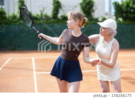 Senior female coach gives tennis lesson, teaches girl game Senior female coach gives tennis lesson, teaches girl game 138288175