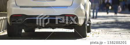 Back view of white car parked on city pedestrian zone on background of blurred silhouettes of people walking along green sunny summer alley. Modern city lifestyle concept. 138288201