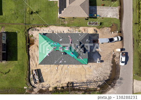 Asphalt shingles being applied to new home rooftop. Roofing workers securing shingles. Florida residential construction site. Asphalt shingles being applied to new home rooftop. Roofing workers securing shingles. Florida residential construction site. 138288231