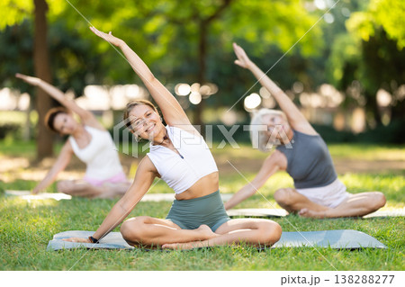 Girl stretching in lotus position group yoga session in park Girl stretching in lotus position group yoga session in park 138288277