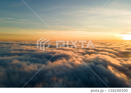 Aerial view of vibrant yellow sunrise over white dense clouds with blue sky overhead. Aerial view of vibrant yellow sunrise over white dense clouds with blue sky overhead. 138288300