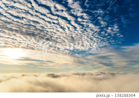 Aerial view of vibrant yellow sunrise over white dense clouds with blue sky overhead. 138288304