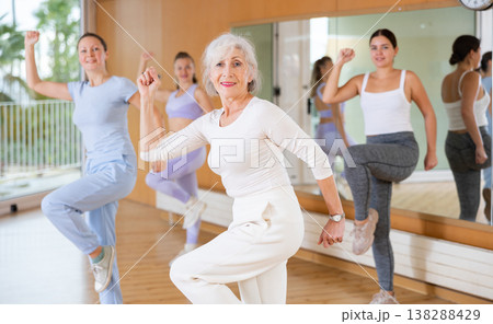 Cheerful senior female choreographer showing new dancing dynamic movements during training together with women in studio 138288429