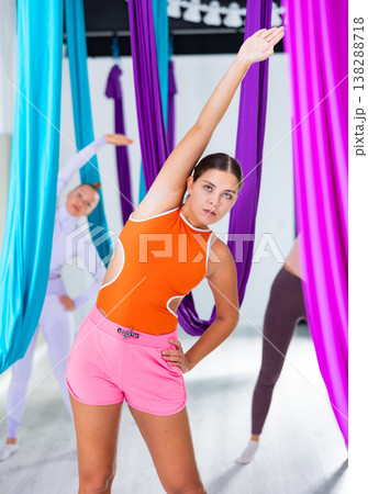 Girl doing articular gymnastics before aerial yoga group training in fitness room Girl doing articular gymnastics before aerial yoga group training in fitness room 138288718