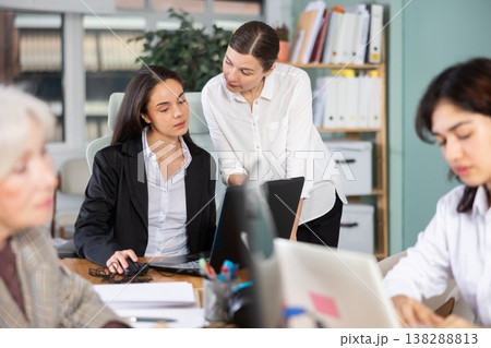 Middle-aged woman helping young colleague with tasks on laptop Middle-aged woman helping young colleague with tasks on laptop 138288813