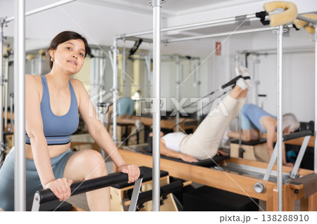 Focused woman performing set of pilates exercises on reformer in fitness studio. Healthy active lifestyle concept Focused woman performing set of pilates exercises on reformer in fitness studio. Healthy active lifestyle concept 138288910