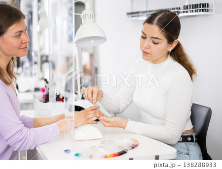 Manicurist files the nails of a young female client 138288933
