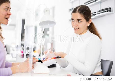 Young female manicurist showing palette of nail varnishes to woman client Young female manicurist showing palette of nail varnishes to woman client 138289002