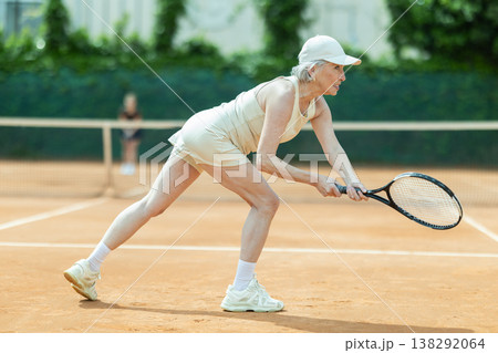Senior female athlete plays tennis on open court with young opponent Senior female athlete plays tennis on open court with young opponent 138292064